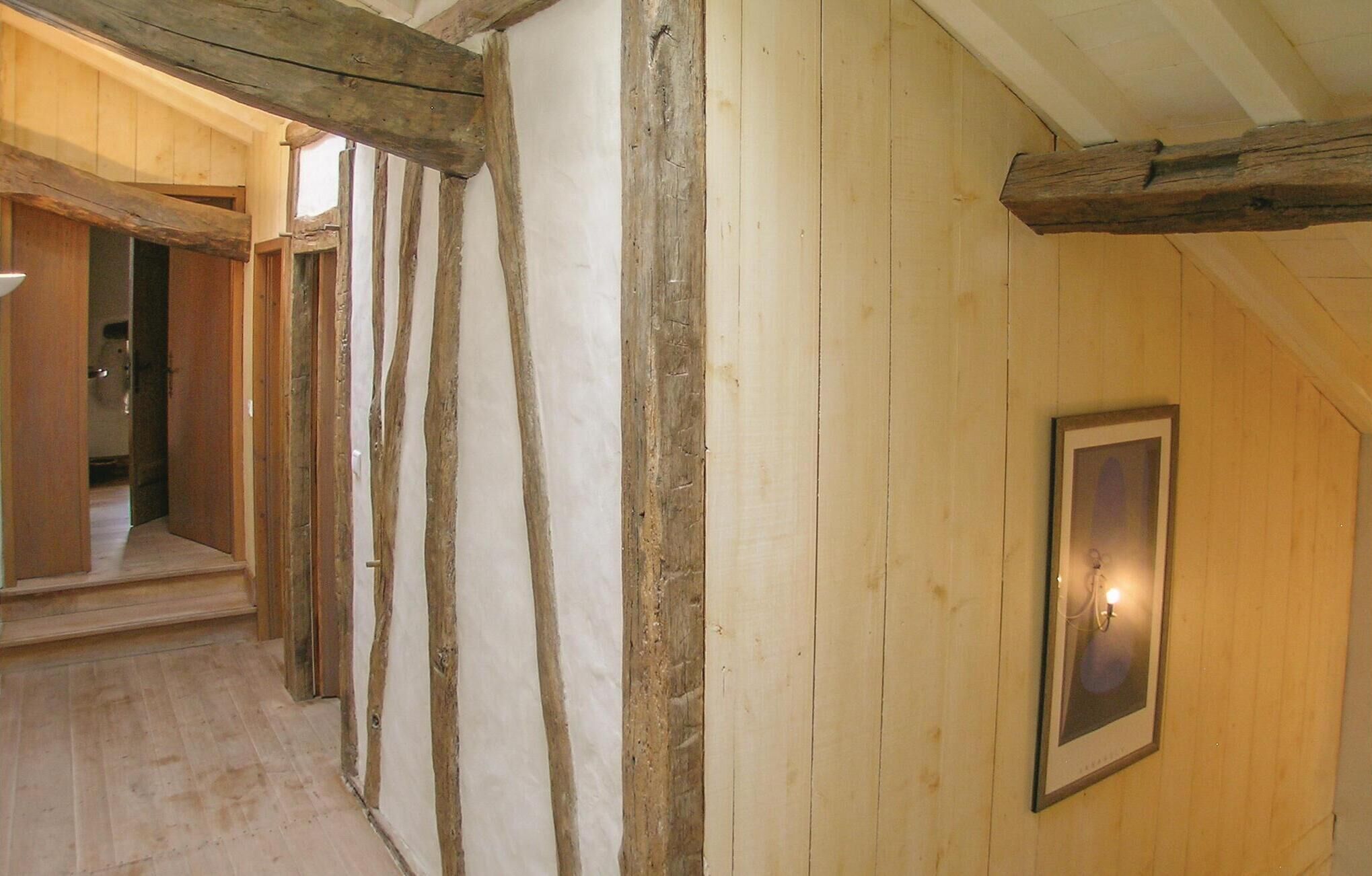 Un couloir avec des poutres en bois apparentes et un tableau encadré accroché au mur.