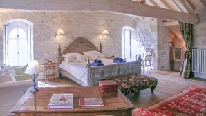 Un dormitorio rústico con una cama de madera, dos lámparas de noche, una caja roja, una mesa de madera con libros y una alfombra roja estampada.