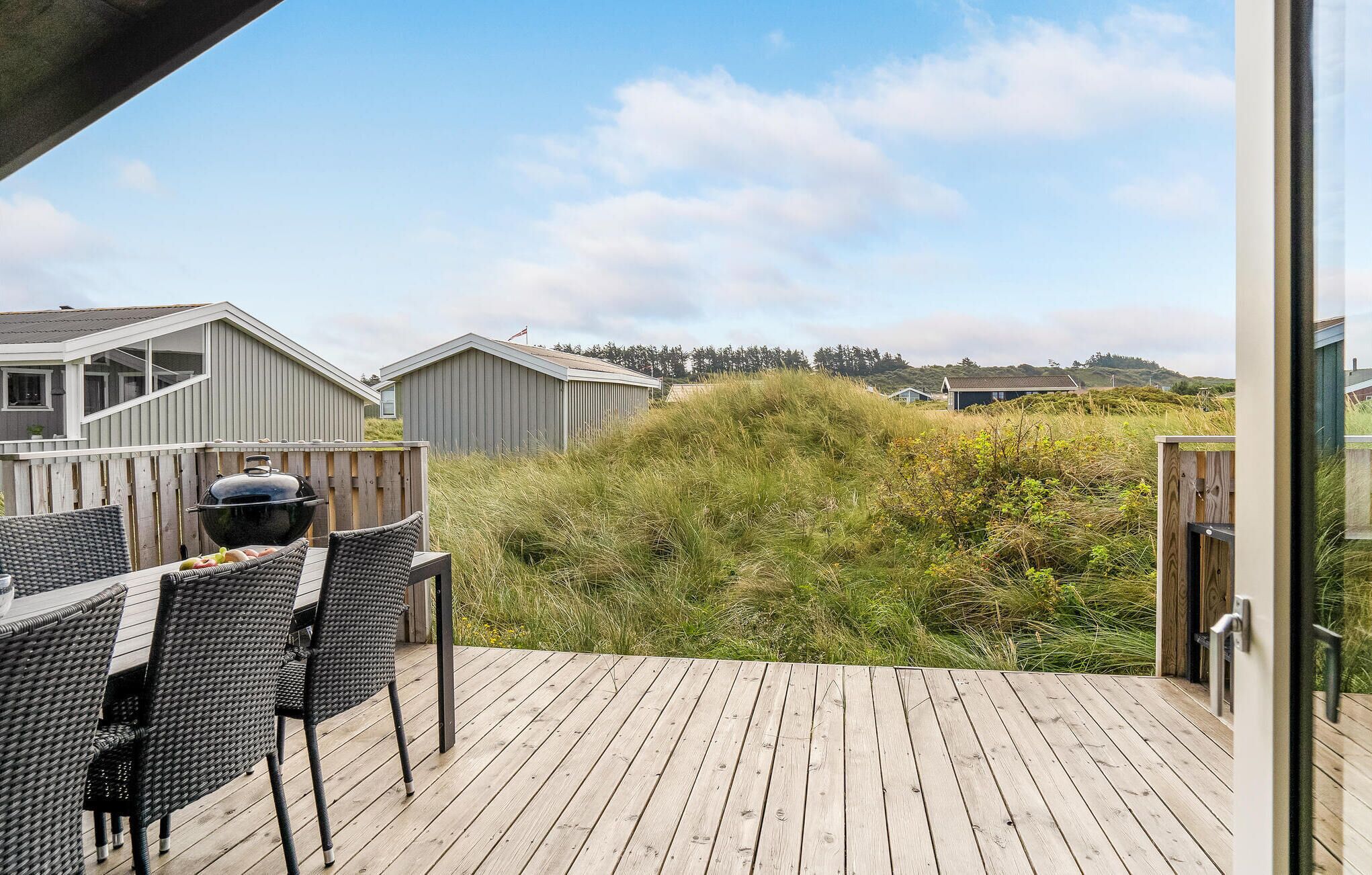 Eine Holzterrasse mit Gartenmöbeln, mit Blick auf eine Rasenfläche und Gebäude im Hintergrund.