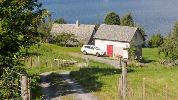 A rural road leading to a white house with a red door, surrounded by greenery and a body of water. - Amazing home in Jondal with WiFi (Jondal)