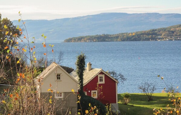 A house with a red and white exterior, situated by a lake with mountains in the background.