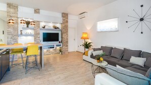 A modern living room with a flat-screen TV, a dining area with yellow chairs, and a cozy seating area with a brown sofa.