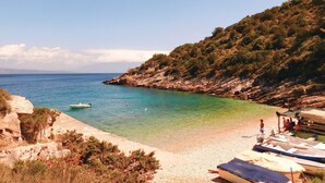 A coastal beach with rocky terrain, clear turquoise waters, and a few boats on the shore.