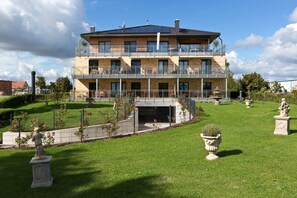 A multi-story building with balconies, a garden with statues, and a clear sky. - Great Ocean - Kells apartments (Klink)