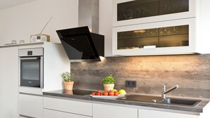 Una cocina moderna con horno empotrado, campana extractora negra, pileta de acero inoxidable y un salpicadero de madera.