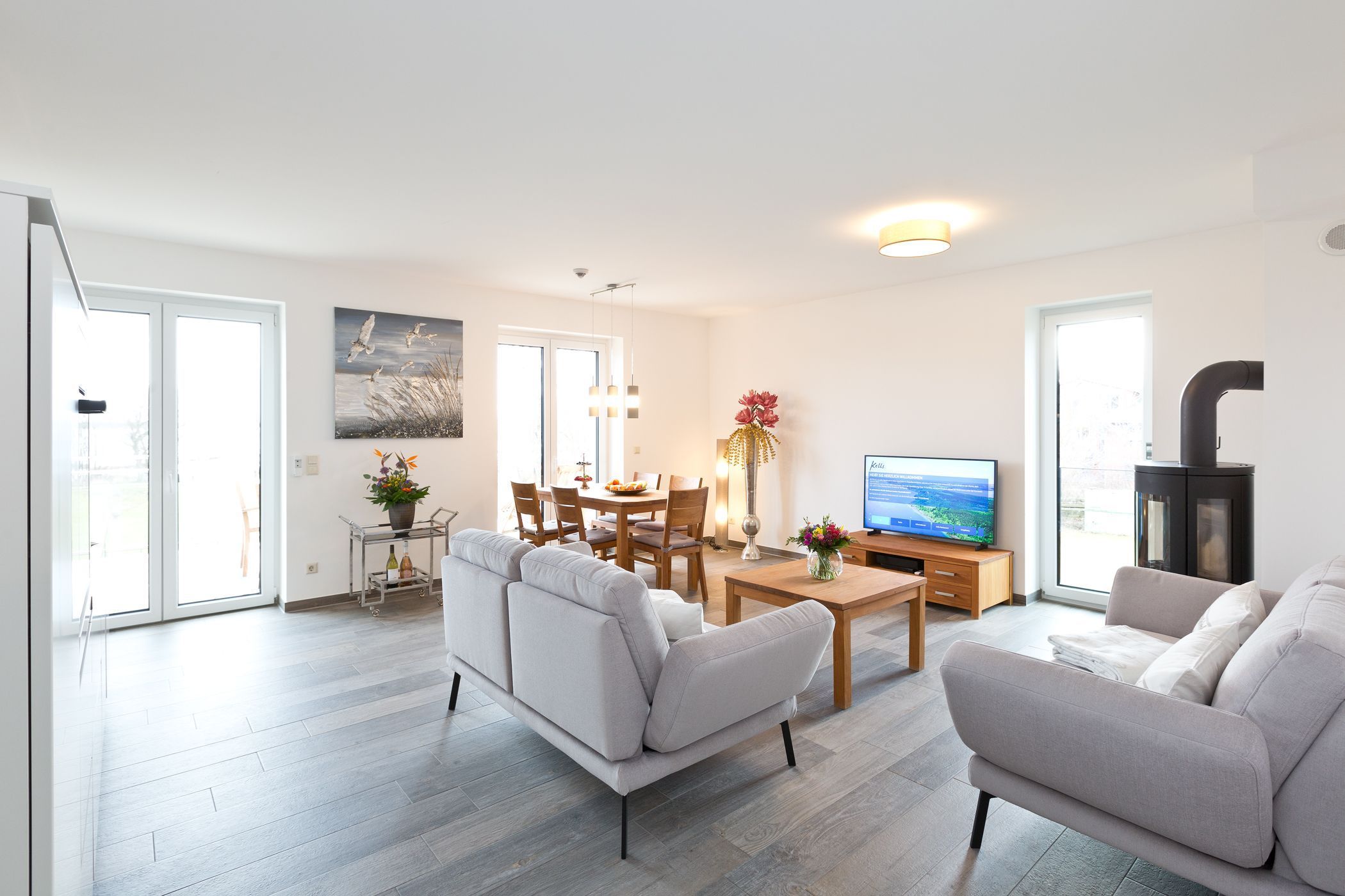 Ein modernes Wohnzimmer mit einer Couch, einem Couchtisch und einem Fernseher. Es gibt einen Essbereich mit Stühlen und einem Tisch, sowie eine Küchenzeile mit einem Herd.