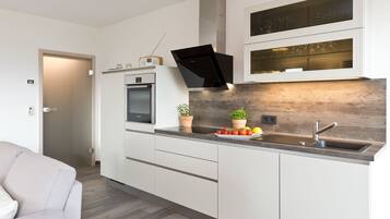 Une cuisine moderne avec des meubles blancs, un four encastré, un four à micro-ondes, une hotte noire et un pare-feu en bois.