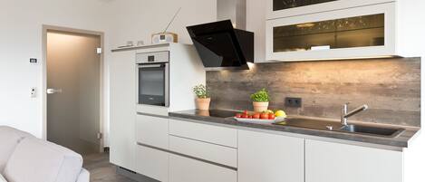 A modern kitchen with white cabinetry, a built-in oven, a microwave, a black range hood, and a wooden backsplash.