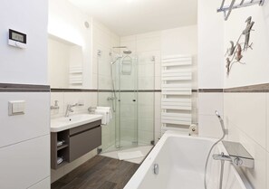 A modern bathroom with a glass-enclosed shower, a bathtub, and a vanity with a sink and mirror. - Great Ocean - Kells apartments (Klink)