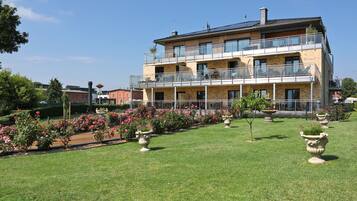 A multi-story building with balconies, surrounded by a well-maintained garden with various plants and flowers.