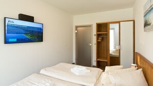 A hotel room with a bed, a TV mounted on the wall, a wooden wardrobe, and a door leading to another room. - Great Ocean - Kells apartments (Klink)