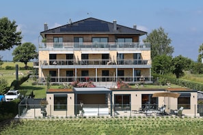 A multi-story building with balconies, a covered outdoor seating area, and a garden.