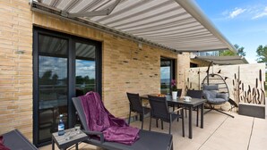 An outdoor patio with a table, chairs, a cushioned lounge chair, and a hanging chair. - Great Ocean - Kells apartments (Klink)