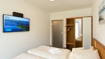 Une chambre d’hôtel avec un lit, un téléviseur fixé au mur, une armoire en bois et une porte donnant sur une autre pièce.