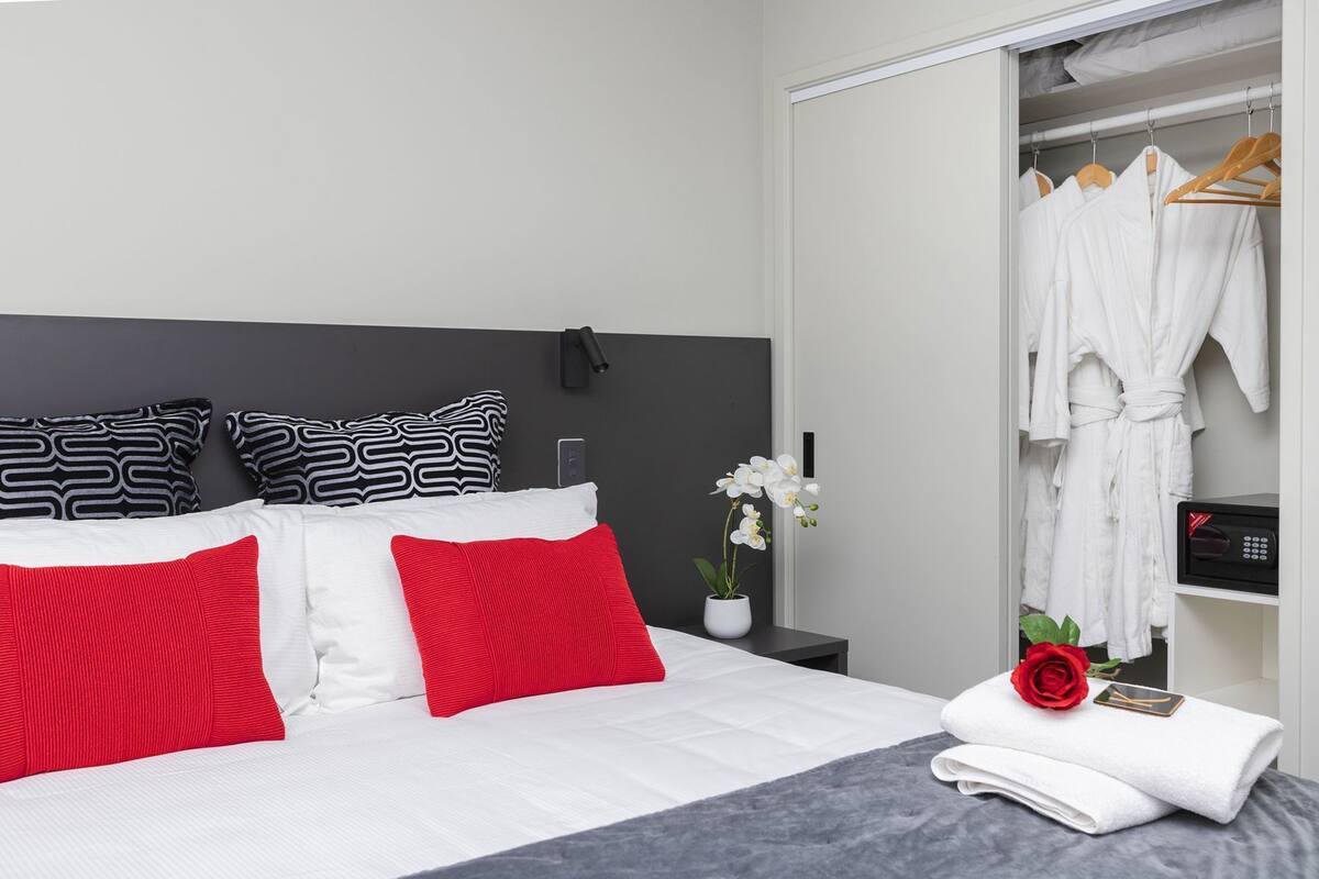 A hotel room with a bed, a wardrobe, a bedside table with a remote control, a potted orchid, and a rose.