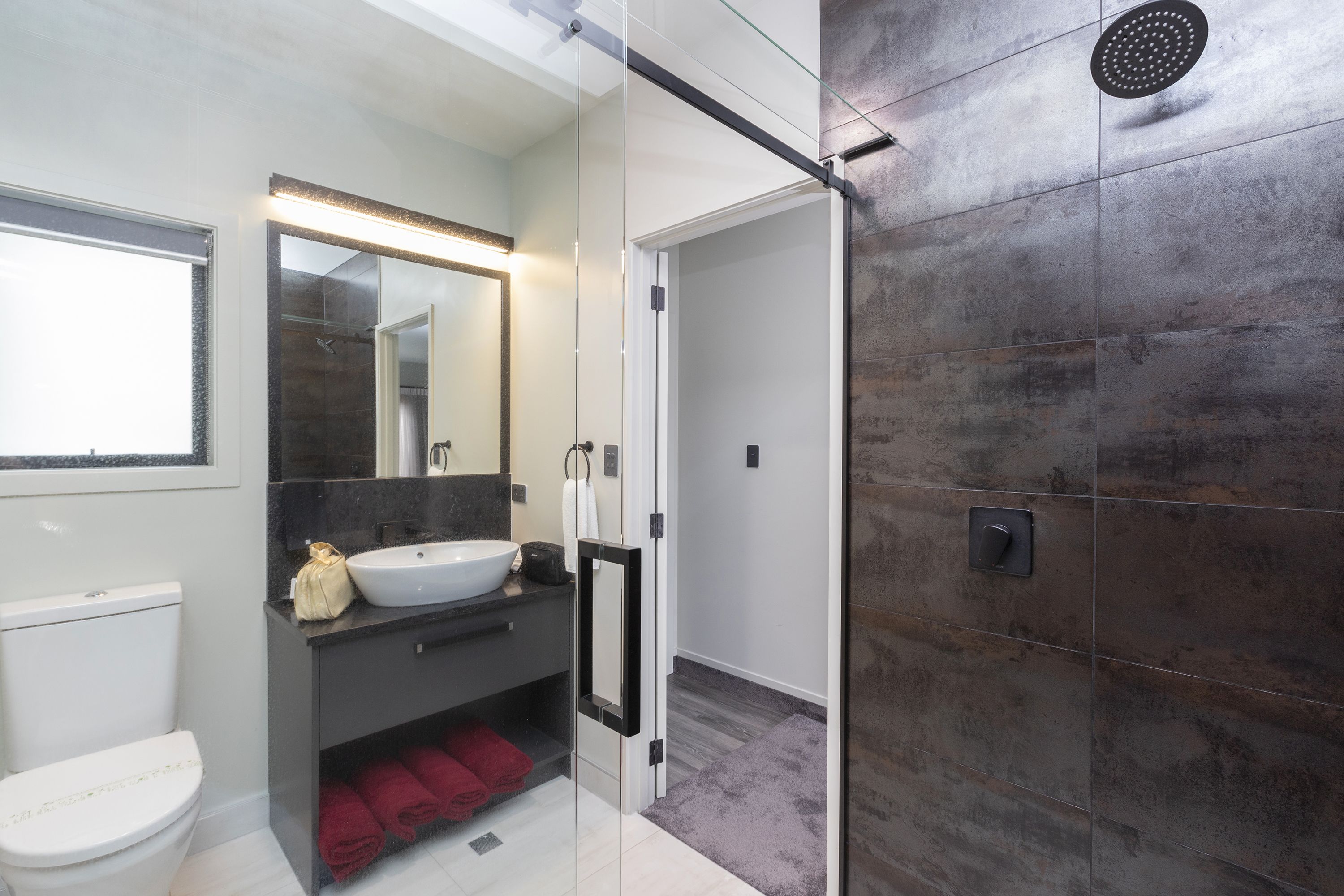A modern bathroom with a glass shower enclosure, a white toilet, a sink with a dark countertop, and a mirror above the sink.