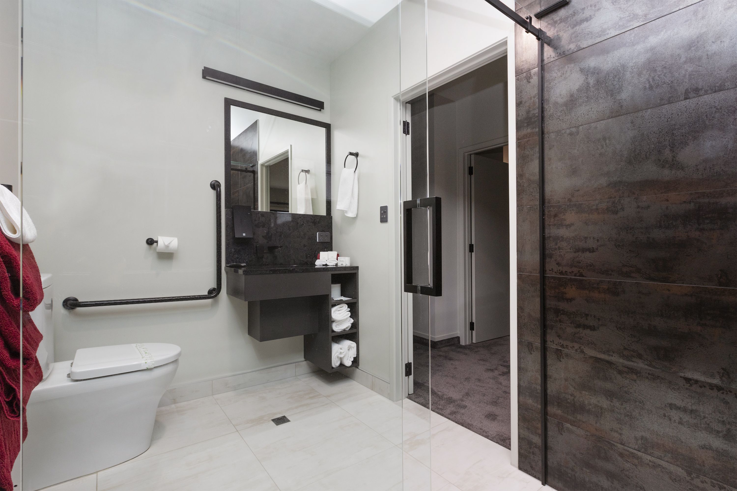 A modern bathroom with a toilet, a vanity with a mirror, and a shower area.