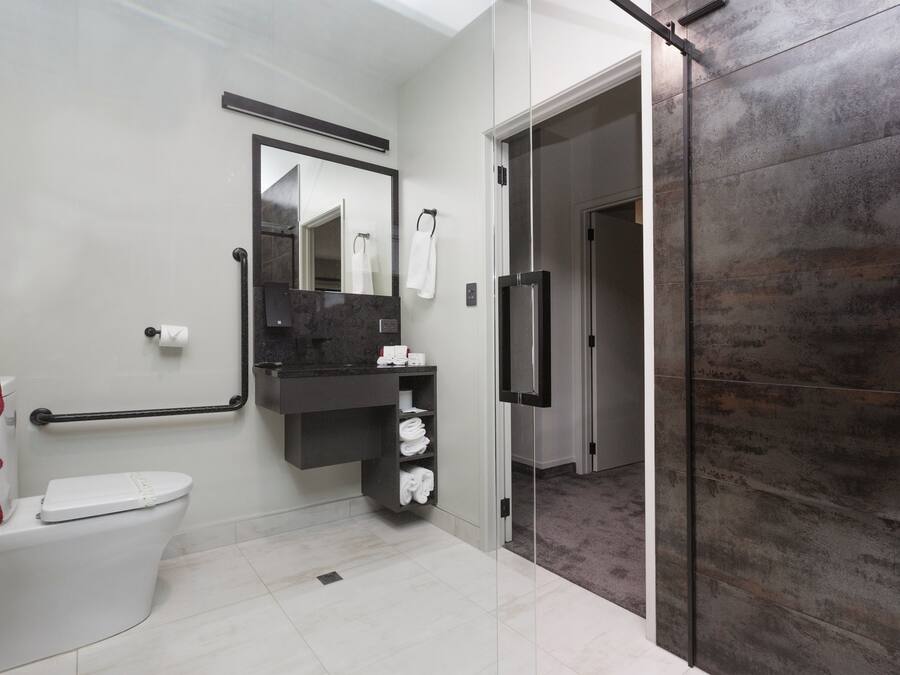 A modern bathroom with a toilet, a vanity with a mirror, and a shower area.