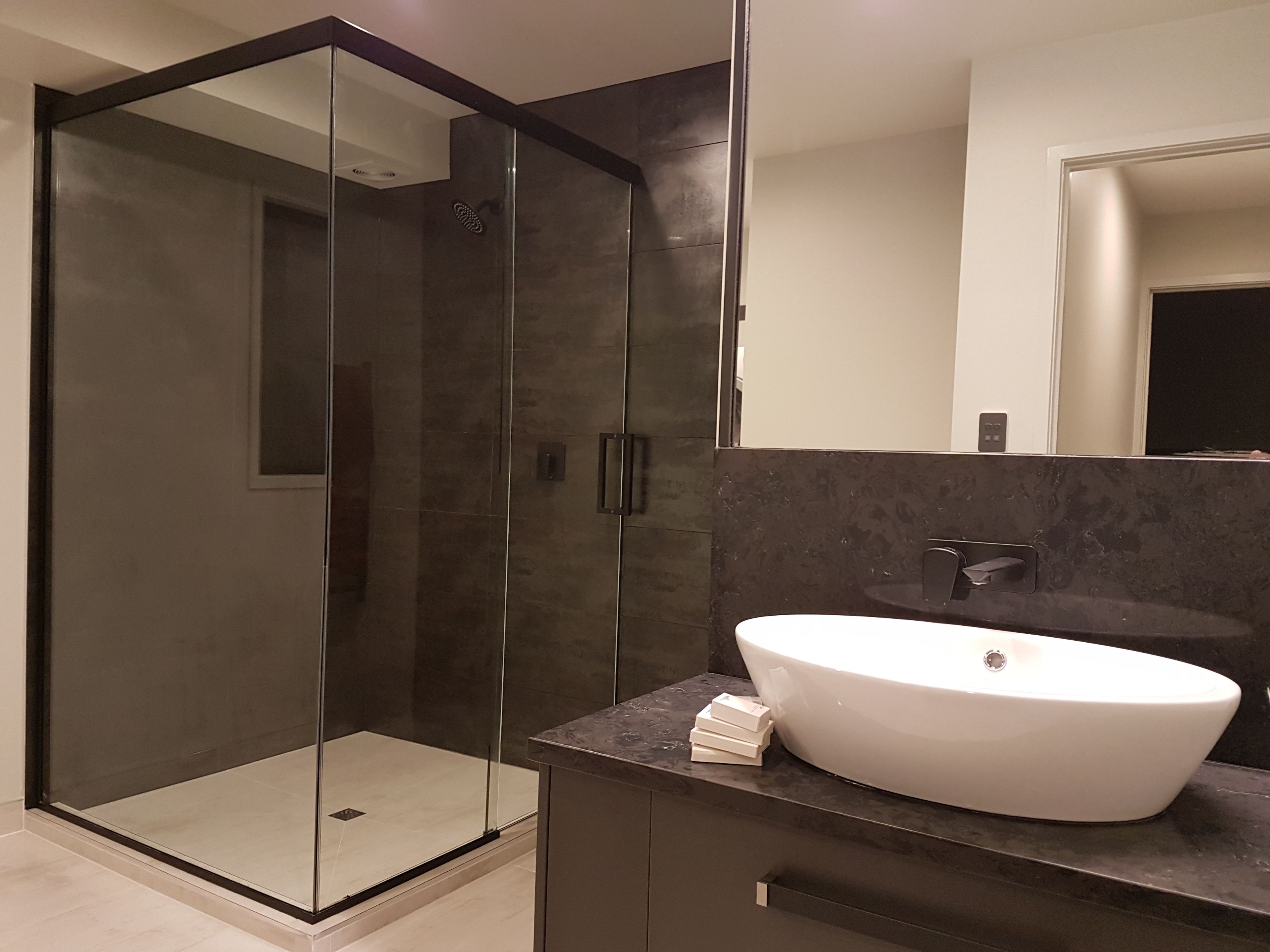 A modern bathroom with a glass-enclosed shower, a white sink, and dark marble countertops.