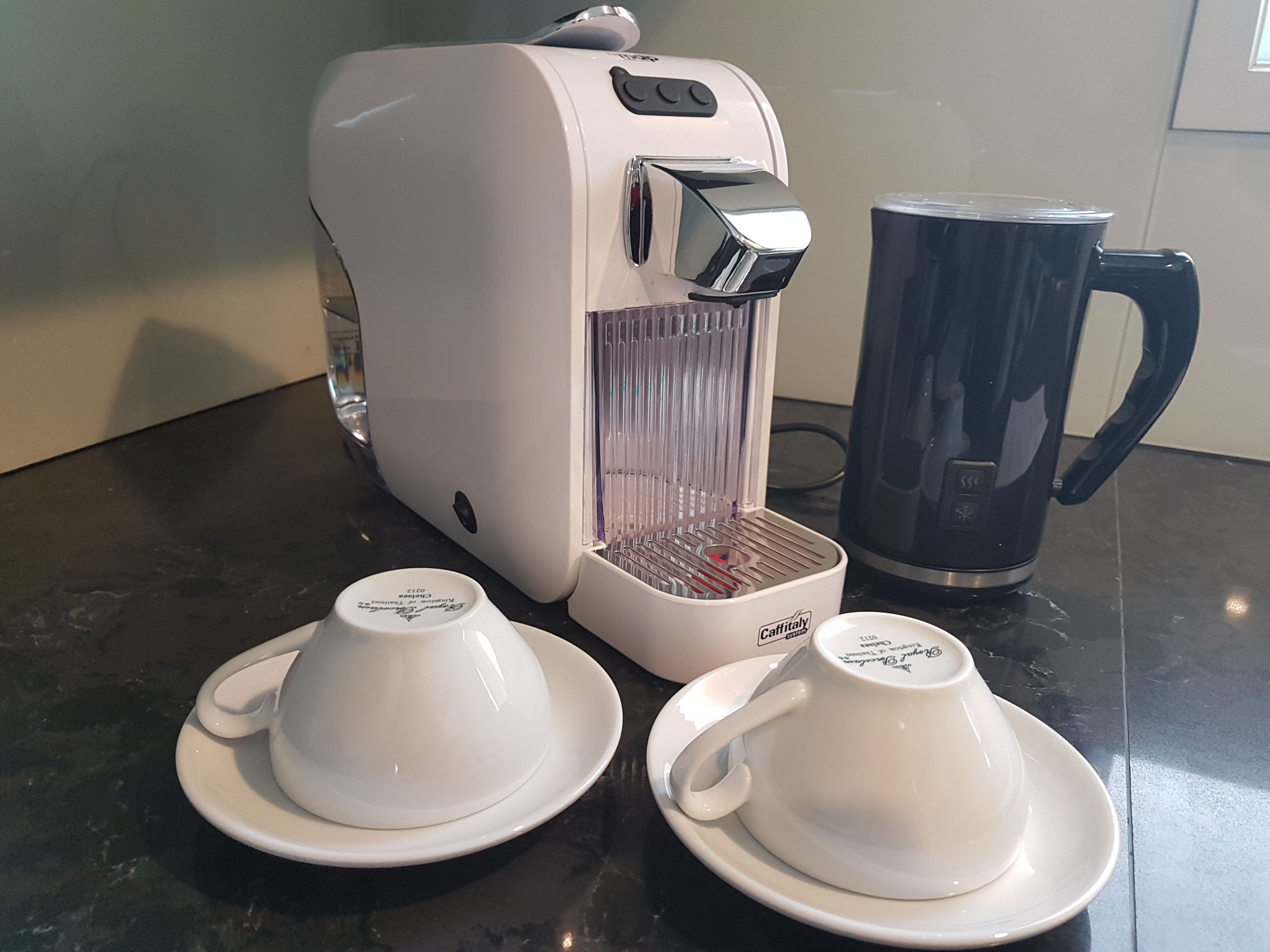 A coffee maker with two white cups on a black countertop.