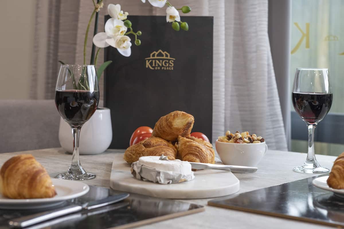 A breakfast setting with croissants, cheese, and a bowl of fruit on a table, accompanied by wine glasses.