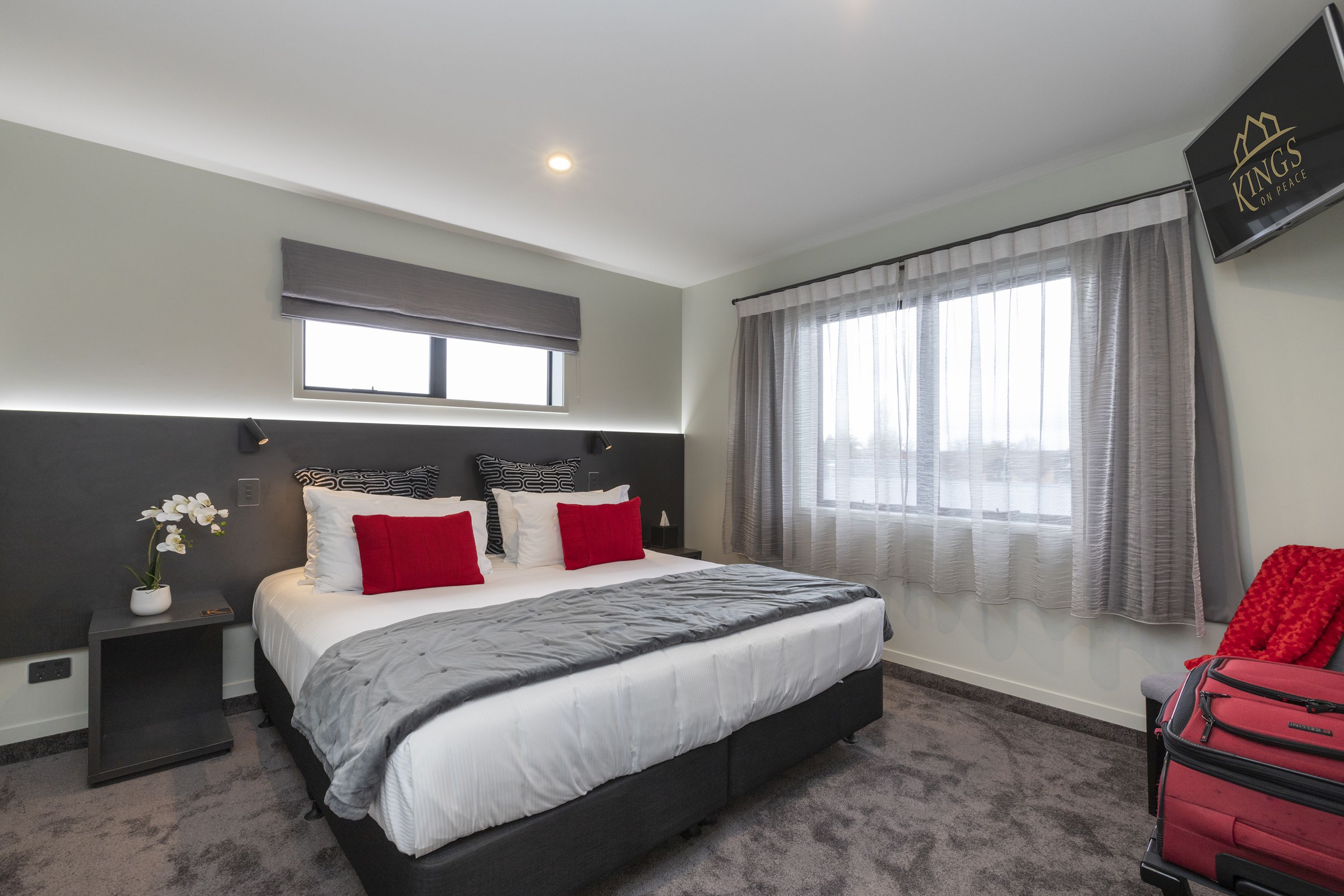 Un dormitorio moderno con una cama grande, una mesita de noche, una silla roja y una ventana con cortinas.