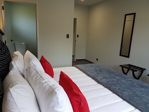 A hotel room with a bed, a grey sofa, a small table, and a mirror on the wall. - Kings On Peace (Rotorua)