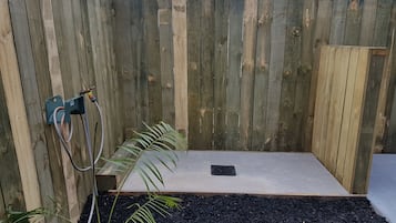 A wooden fence with a concrete shower area, a metal hose, and a black drainage grate.