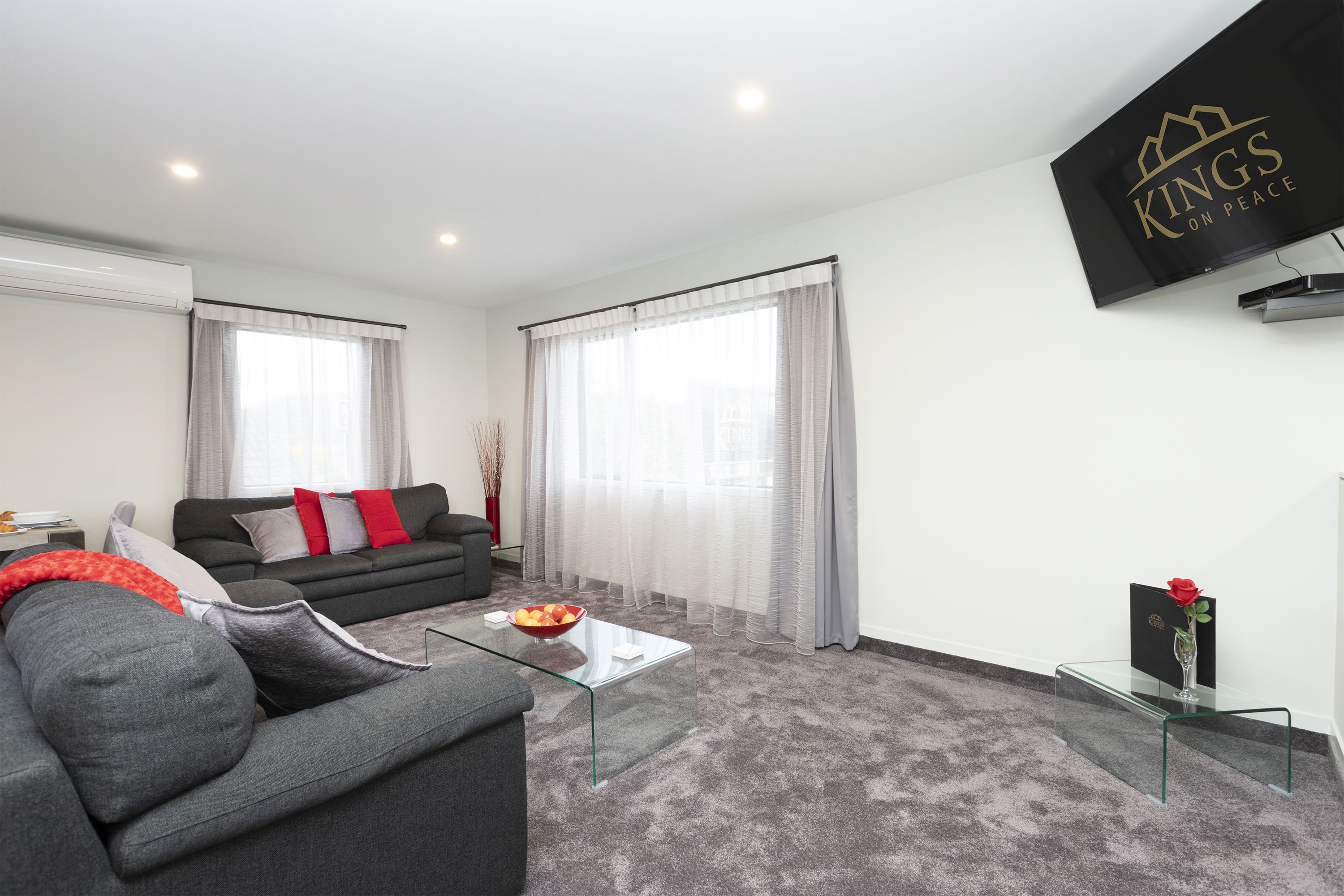 A modern living room with a grey sofa, a glass coffee table, and a black TV on the wall.
