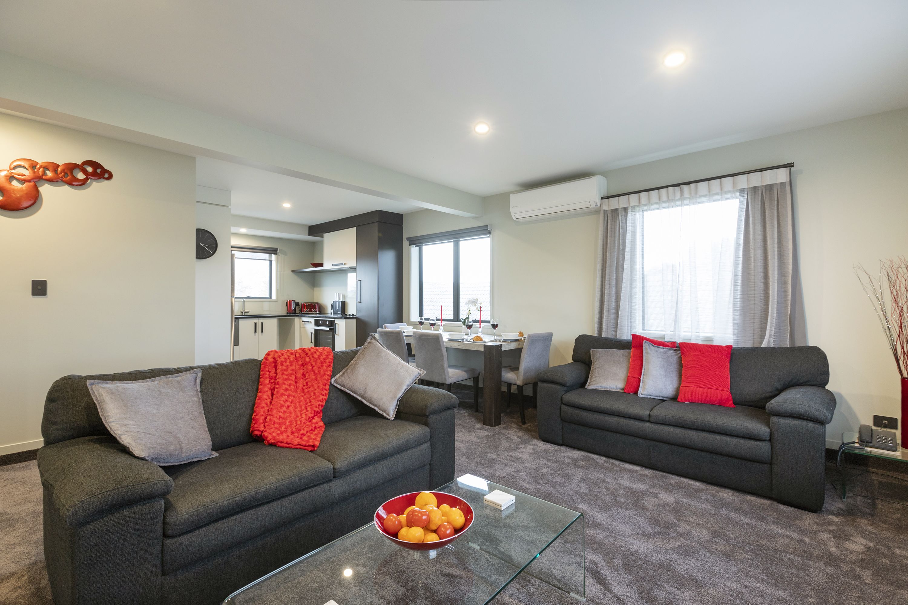 A modern living room with two grey sofas, a glass coffee table, and a dining area in the background.