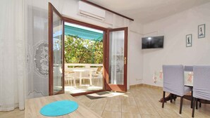 A room with a wooden table, a TV mounted on the wall, and a sliding glass door leading to an outdoor area with a patio and chairs. - Holiday apartment mit Terrasse und Klimaanlage (Baška)