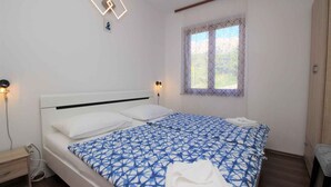 A neatly made bed with a geometric patterned bedspread, a bedside table with a lamp, and a window with lace curtains. - Holiday apartment mit Terrasse und Klimaanlage (Baška)