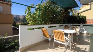 An outdoor patio with a table and chairs, a green umbrella, and a view of mountains. - Holiday apartment mit Terrasse und Klimaanlage (Baška)