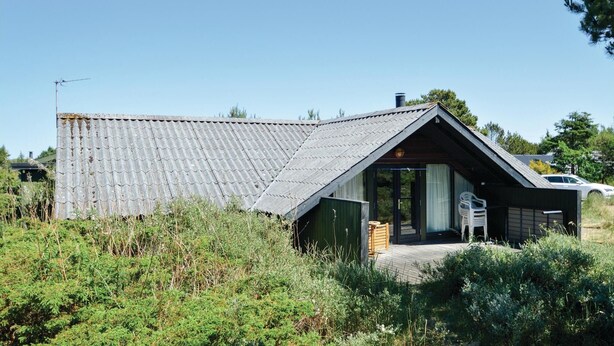 Una casa moderna con techo inclinado, terraza de madera y un pequeño porche con una silla.