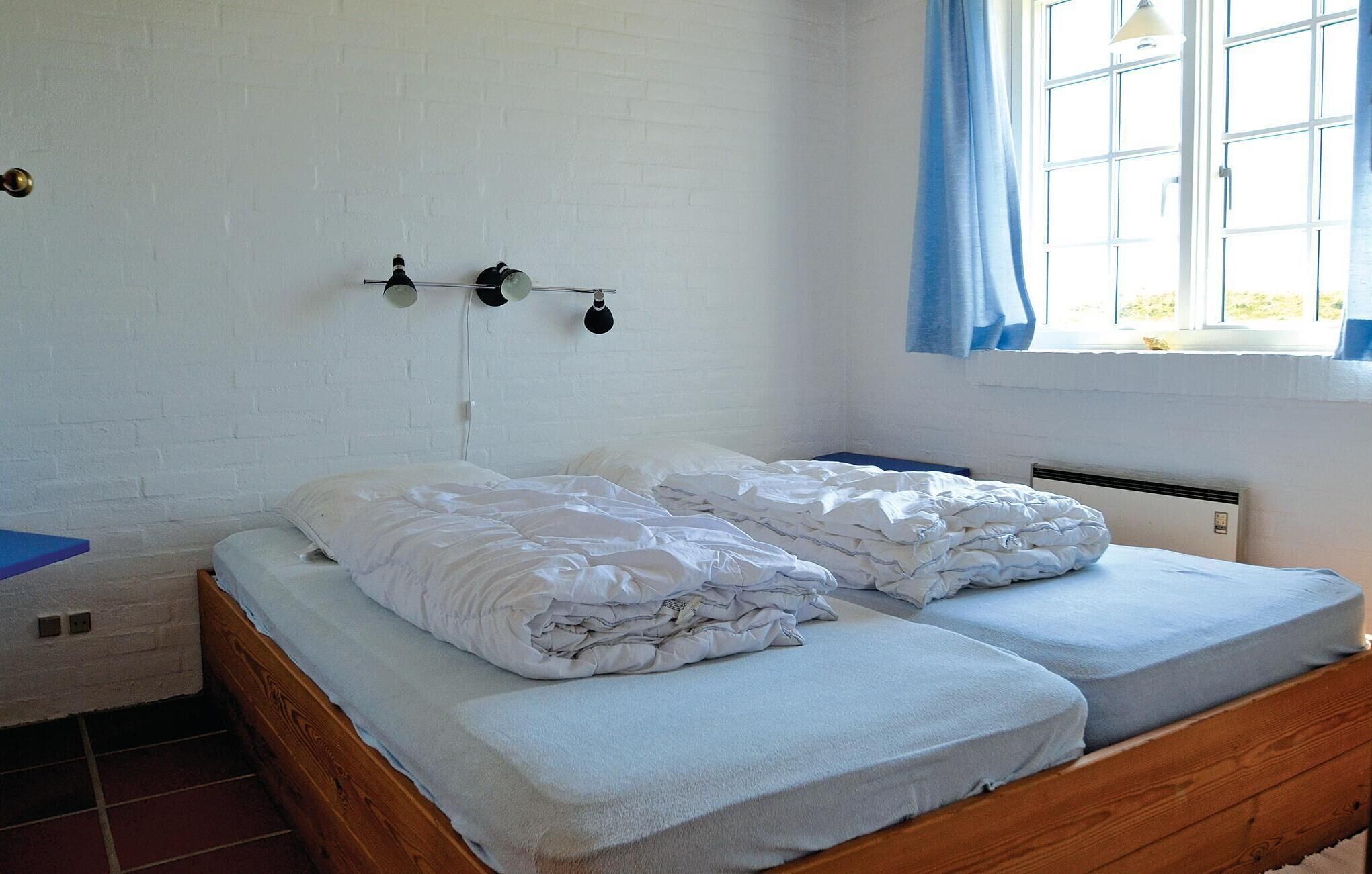 A room with a double bed, a small table, a window with curtains, and a brick wall.