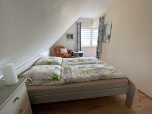 Une chambre à coucher avec un lit, une chaise, une petite table et une fenêtre avec des rideaux.