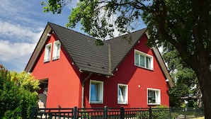 Ein rotes Haus mit einem steilen Dach, einem schwarzen Zaun und einem Baum im Vordergrund.