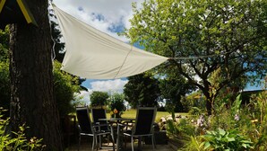 Eine Terrasse im Freien mit Tisch und Stühlen, umgeben von Grünpflanzen und Bäumen.
