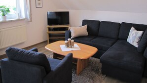 Una sala de estar moderna con un sofá modular, una mesa de centro de madera, un televisor de pantalla plana y una lámpara de techo.