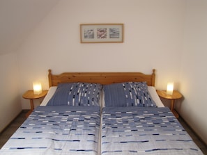 Ein Doppelbett mit blau-weißer Streifenoptik, zwei Nachttische mit Lampen und ein gerahmtes Bild an der Wand.