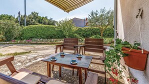 Eine Außenpatio mit Holztisch und -stühlen, umgeben von viel Grün und einem Gebäude, an dem ein Schild mit der Aufschrift „PIZZA & CAFE“ steht.
