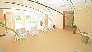 A spacious room with three white lounge chairs, a large window, and a potted plant.