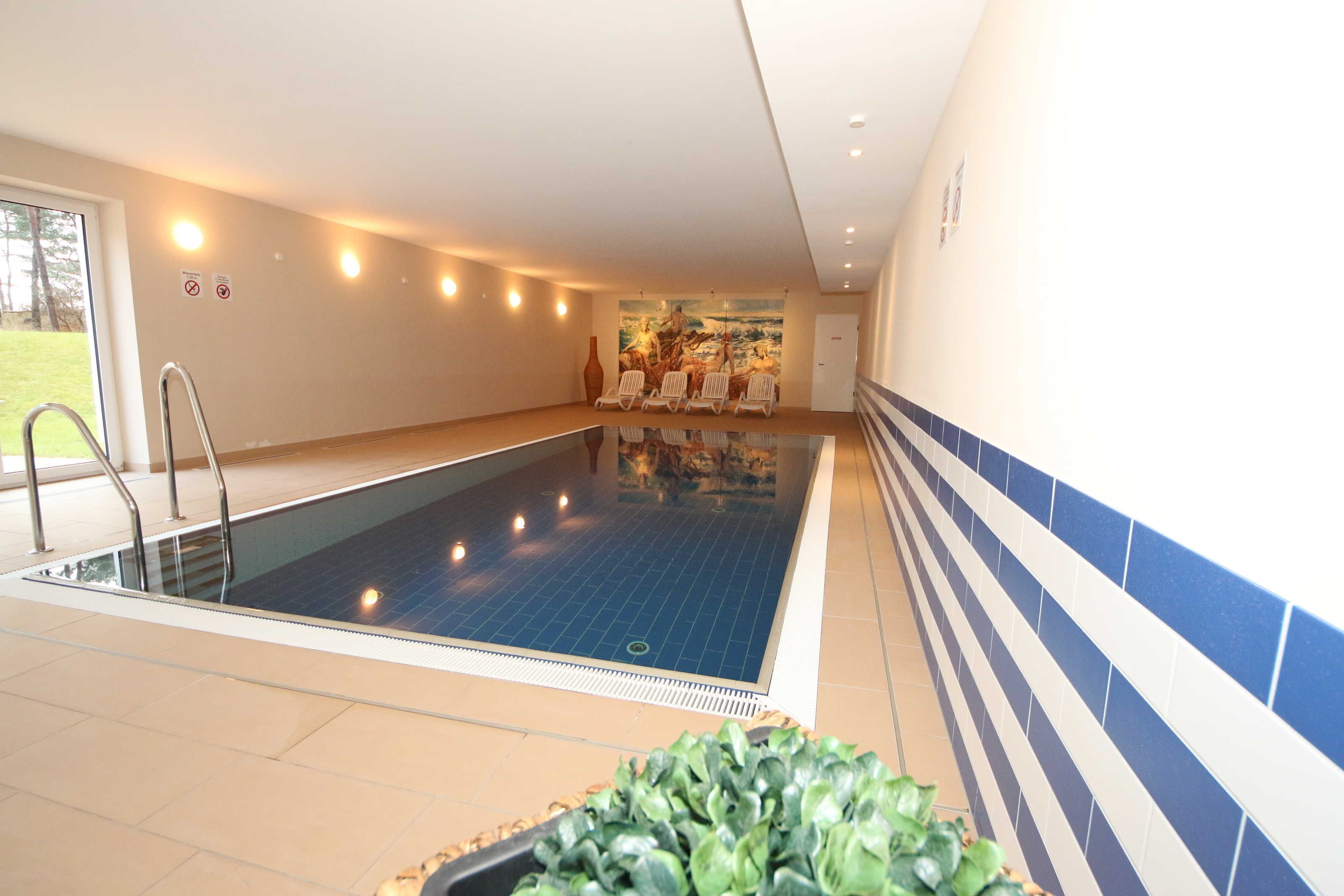 Une piscine intérieure avec un sol carrelé, une échelle en métal et un espace détente avec des chaises.