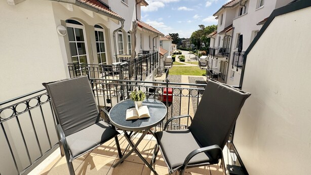 A balcony with two chairs and a table, overlooking a courtyard with buildings and a street.