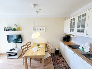 A compact kitchen with a dining table, chairs, a TV, and a small shelf with books and decorative items. - F: House Meeresblick A 2.09 Island paradise with balcony - House Meeresblick A 2.09 (Baabe)