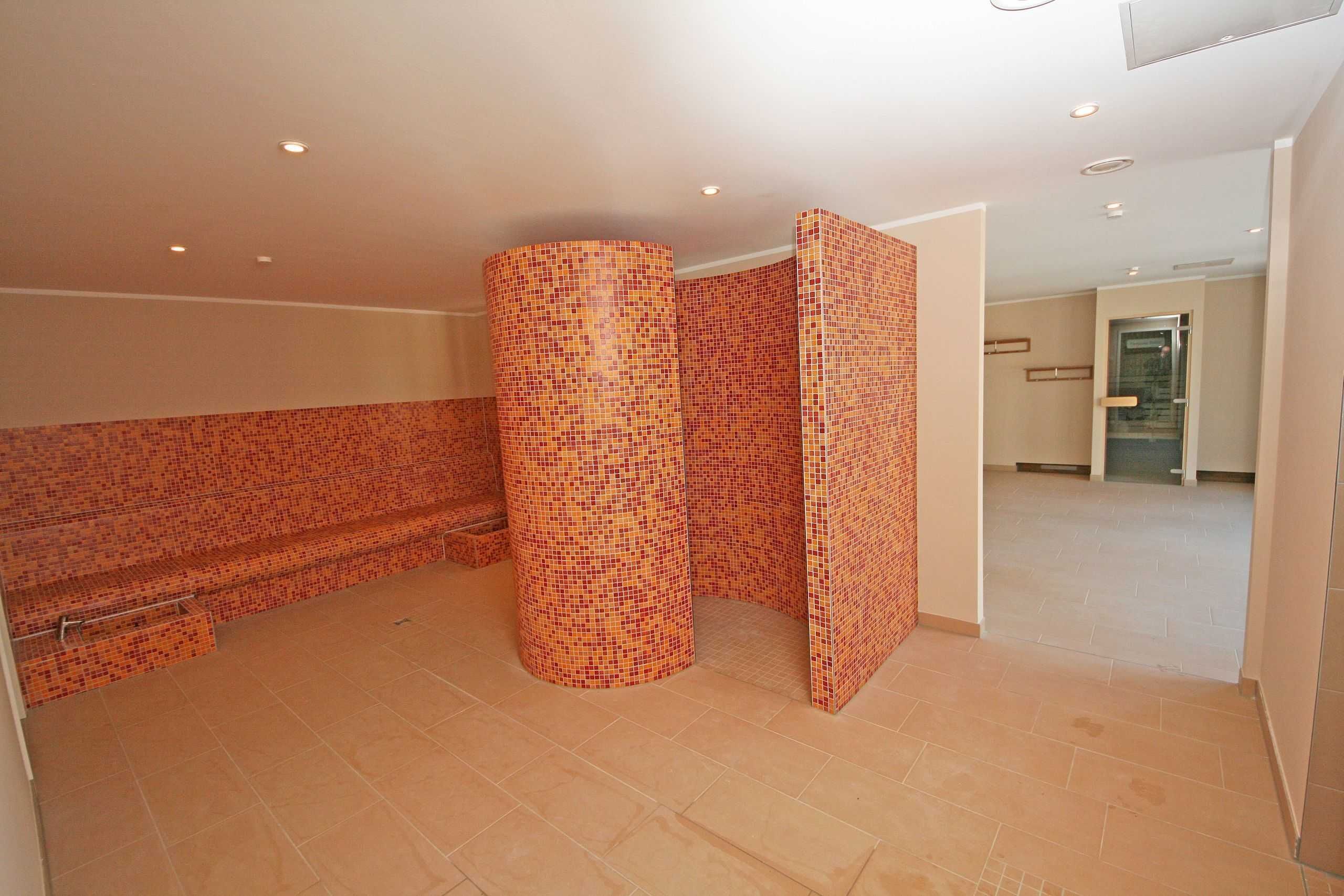 A spa area with tiled walls and floor, a bench, and a glass door leading to another room.