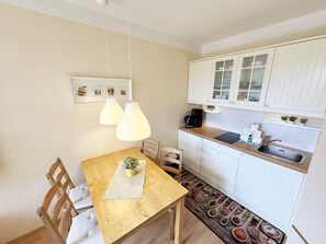 A compact kitchen with white cabinets, a wooden dining table, and pendant lights. - F: House Meeresblick A 2.09 Island paradise with balcony - House Meeresblick A 2.09 (Baabe)