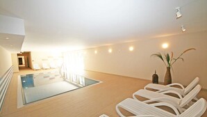 A spacious indoor pool area with a clear view of the pool, lounge chairs, and a potted plant.
