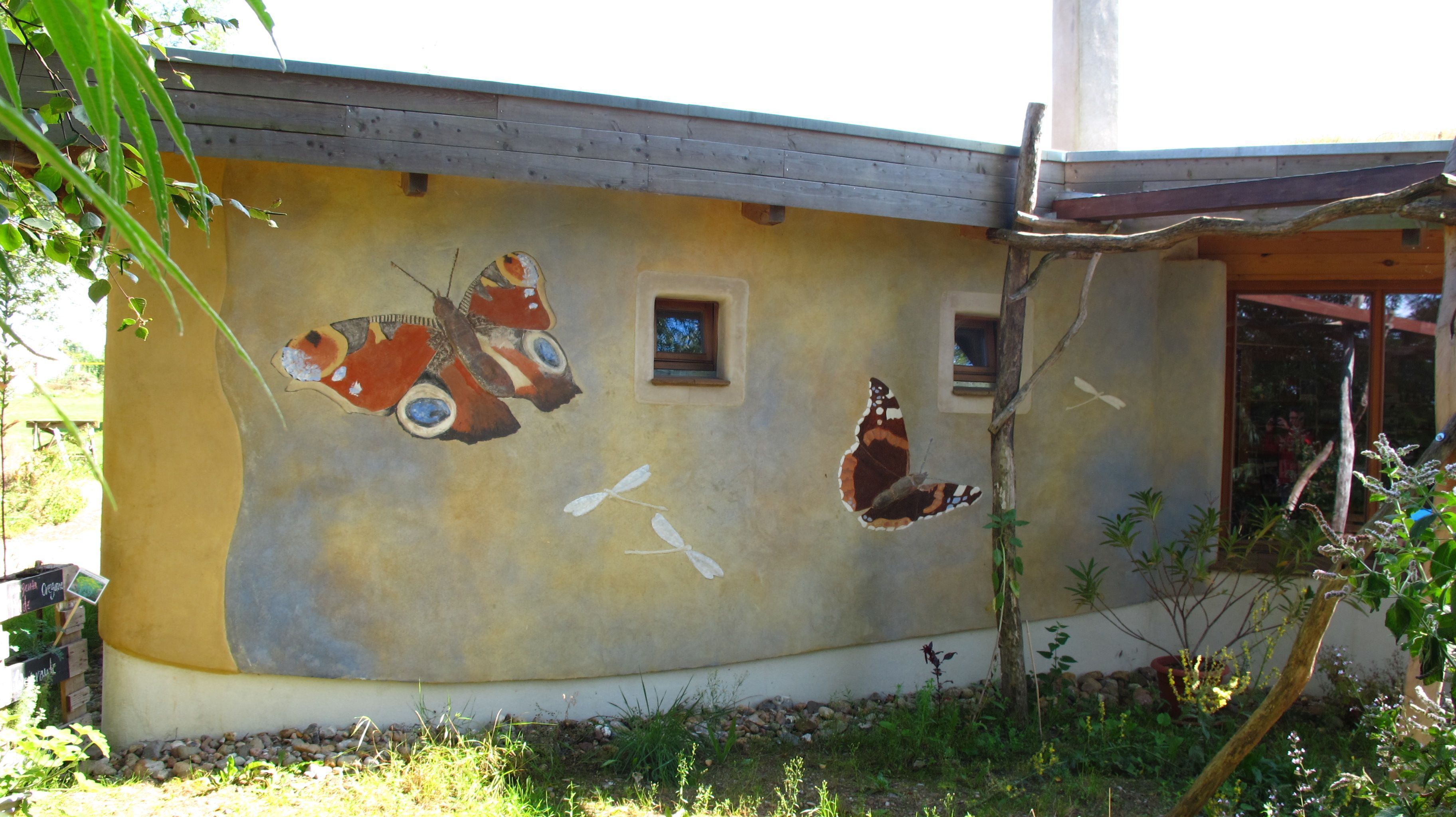 A building with a mural of butterflies and birds, a small window, and a wooden structure.
