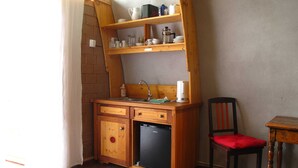 Une cuisine compacte équipée d’un évier, d’un petit réfrigérateur et d’étagères en bois au-dessus du plan de travail.